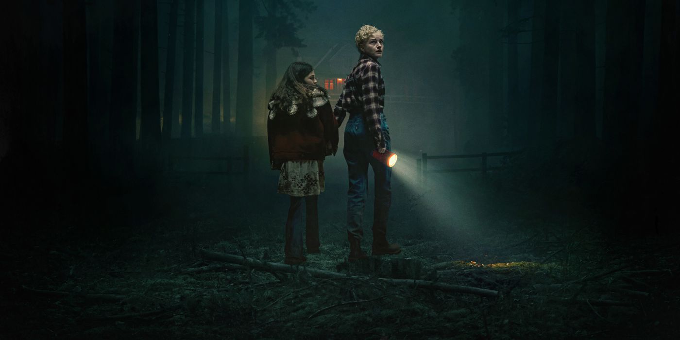 Julia Garner and Matilda Firth as Charlotte and Ginger walking in the woods with a flashlight on the poster for Wolf Man.