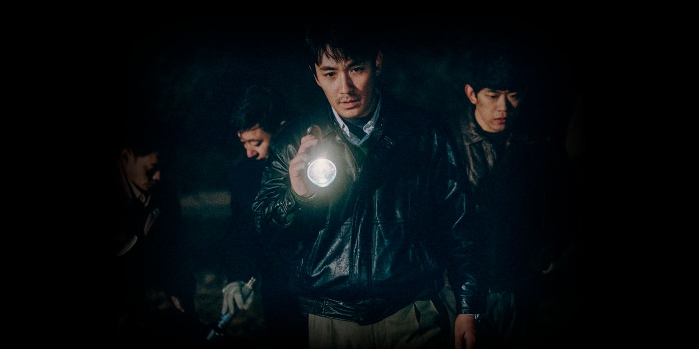 A group of men are looking around in the dark, with the man in the center pointing a flashlight to something in front of him that's off-screen