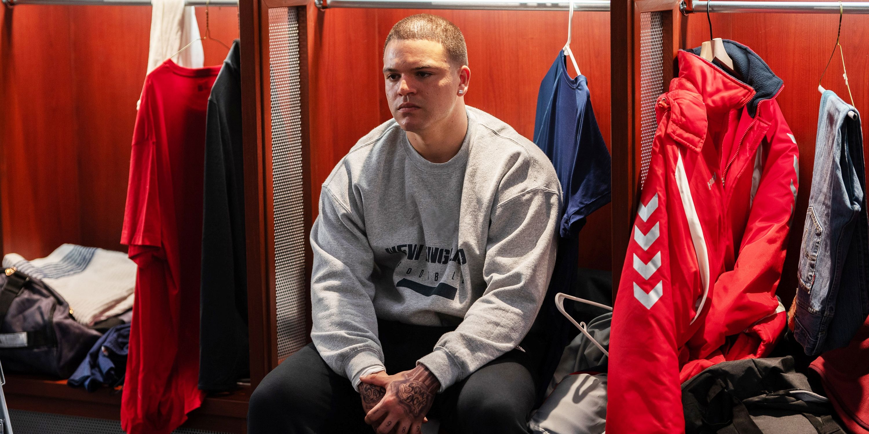 Josh Rivera as Aaron Hernandez looking defeated while sitting in the locker room in American Sports Story