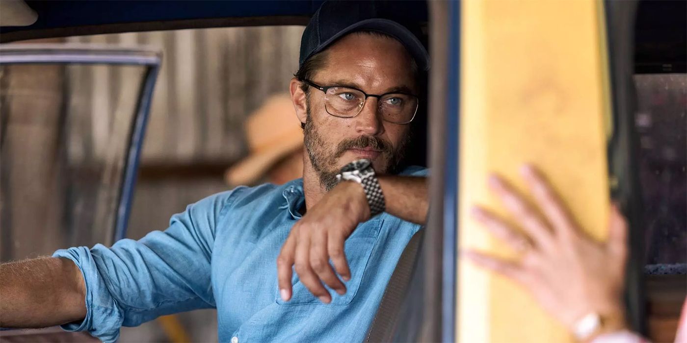 Travis Fimmel with his arm over the back of a truck seat, wearing glasses, and looking at someone