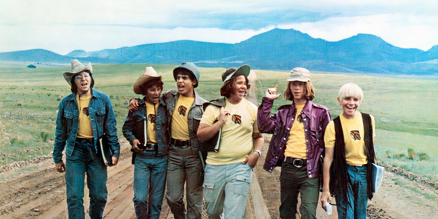 The cast walk down a road with mountains behind wearing matching shirts in Bless the Beasts and Children.