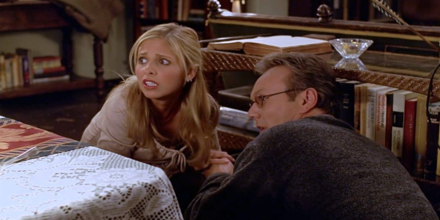 Giles (Anthony Head) and Buffy (Sarah Michelle Gellar) hide behind a table in Buffy the Vampire Slayer.