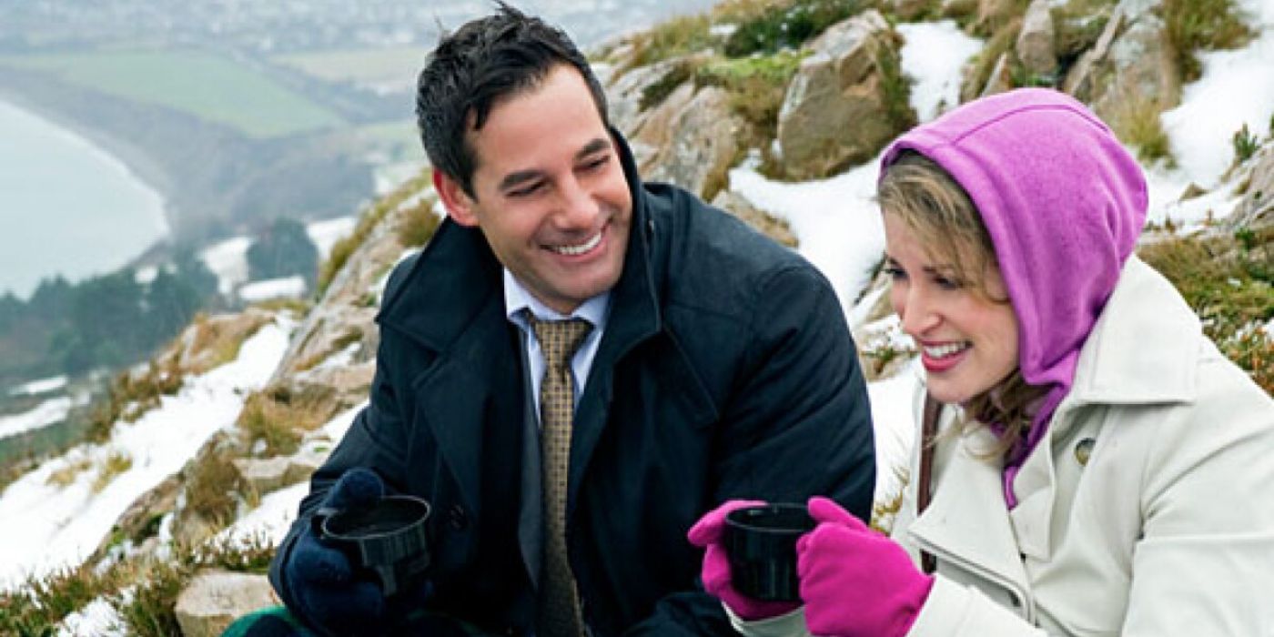 Adrian Pasdar as Michael and Amy Huberman as Sarah laughing on a snowy cliff in Chasing Leprechauns.