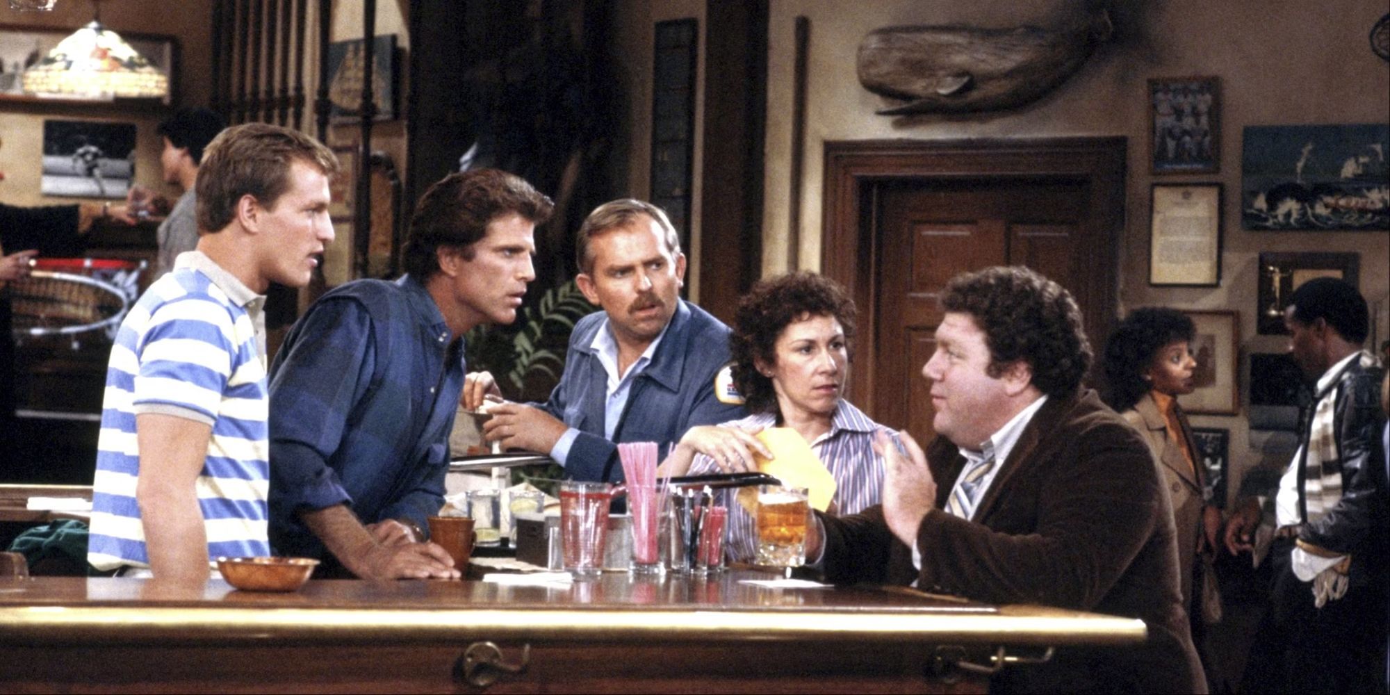 Some of the main cast gather around the bar and listen to Norm talk in Cheers.