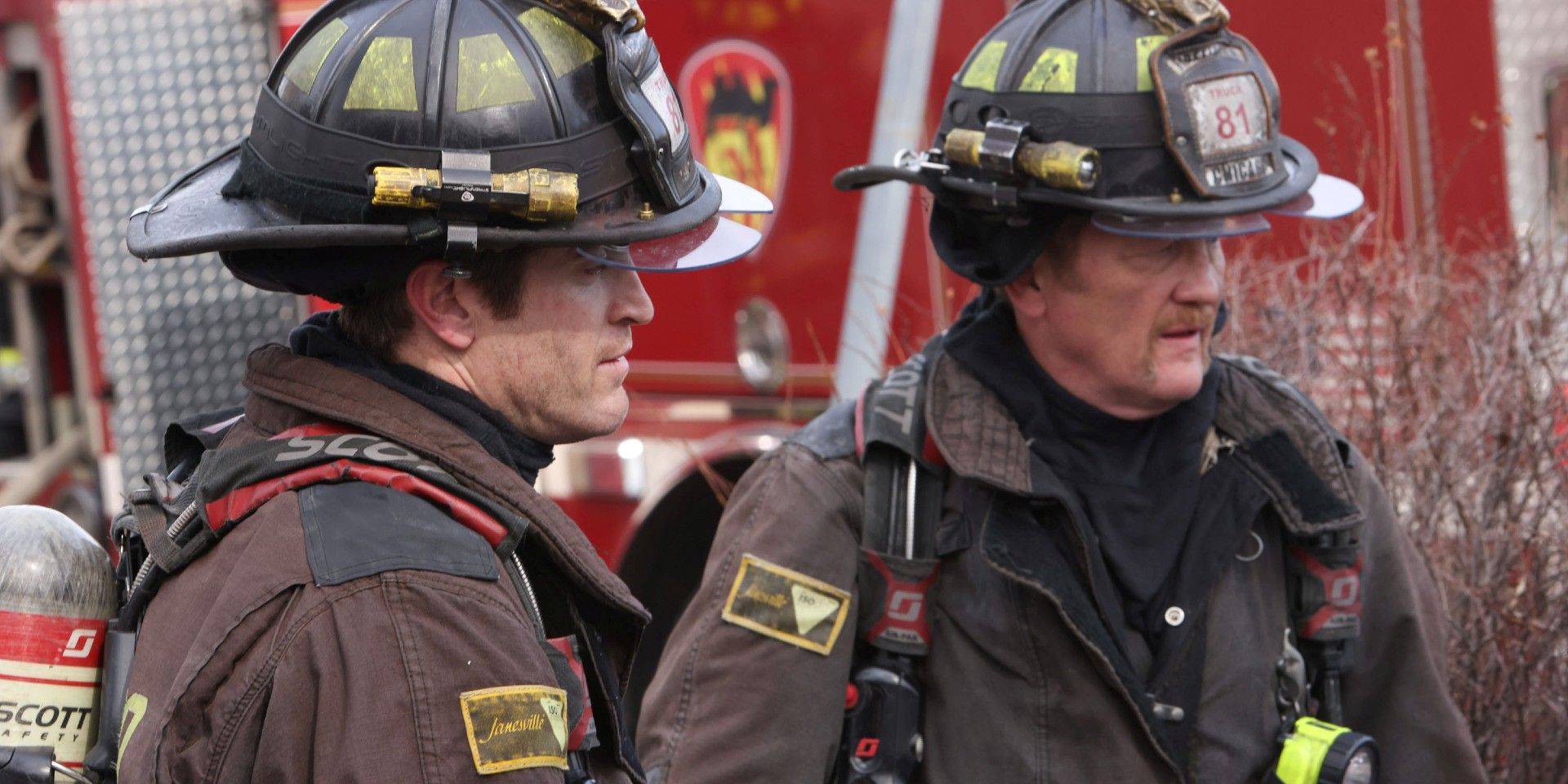 Two firemen stand in their gear next to a fire truck in Chicago Fire