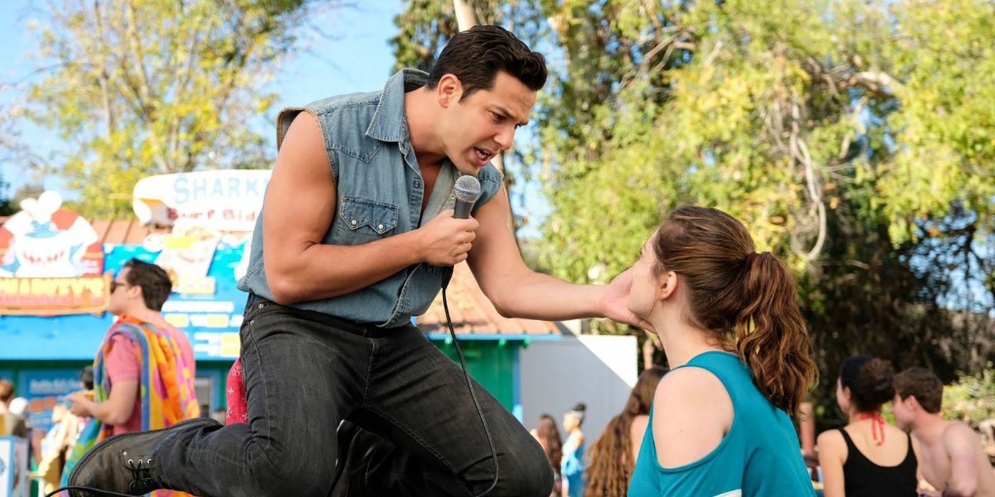 Skyler Astin in a jean vest on his knees singing to a woman in Crazy Ex-Girlfriend