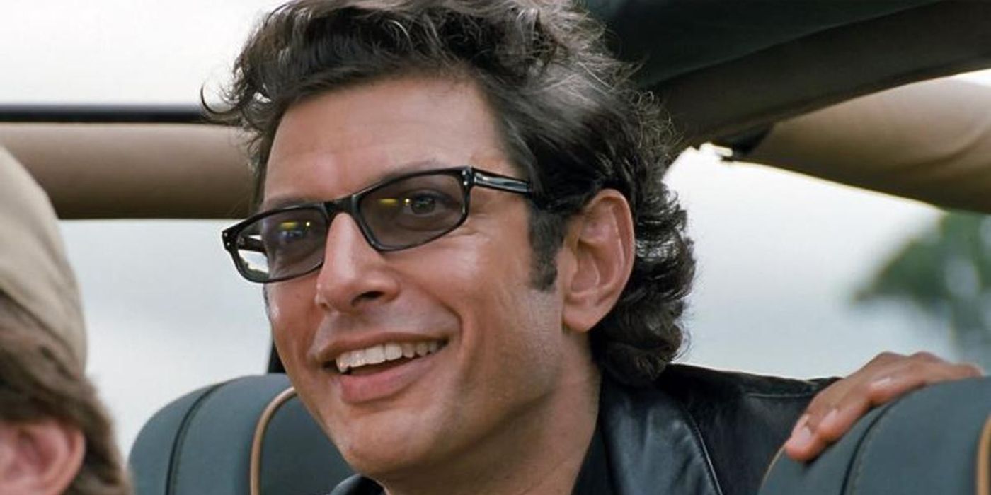 Dr. Ian Malcolm (Jeff Goldblum) smiles joyously as he peers through the front window of a car in &lsquo;Jurassic Park&rsquo; (1993).