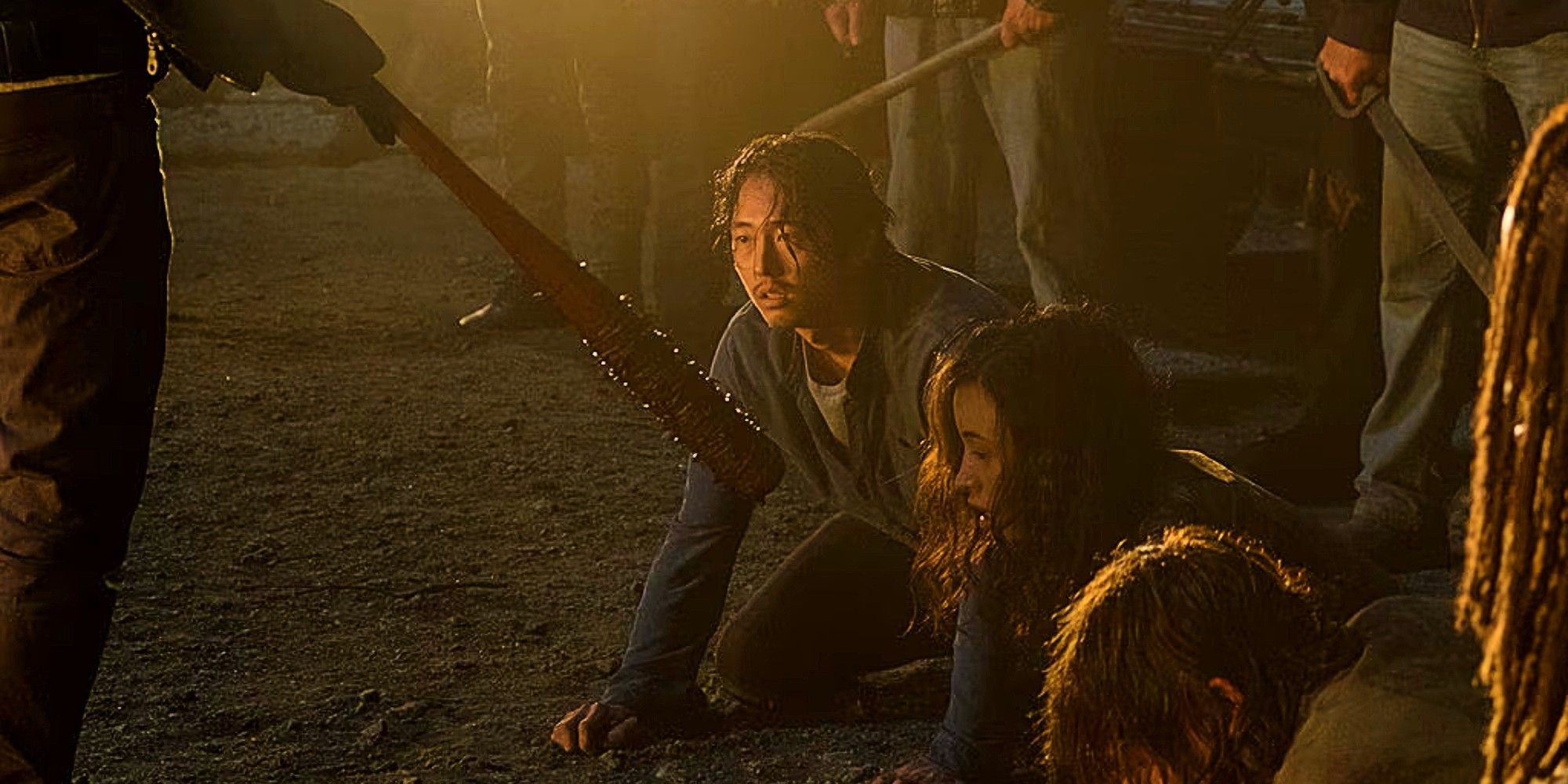 Glenn Rhee crouched down as Negan stands out of frame, holding a bat, in The Walking Dead.