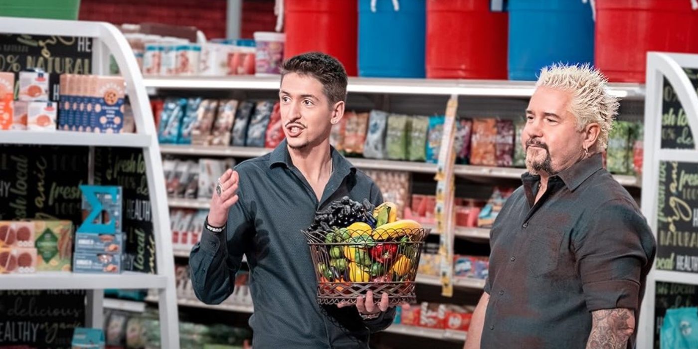 A contestant holds a basket of fruit and stands next to host Guy Fieri on Guys Grocery Games.