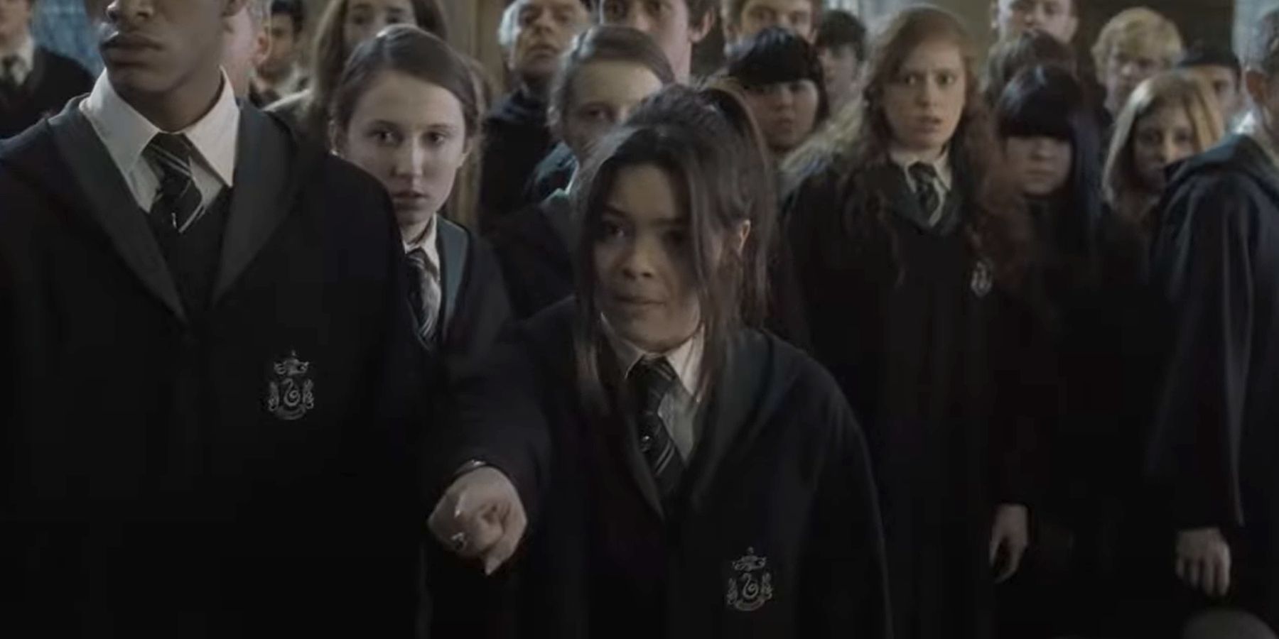 Scarlett Byrne as Pansy Parkinson in Harry Potter and the Deathly Hallows Part 2, standing in a crowd of students and pointing.