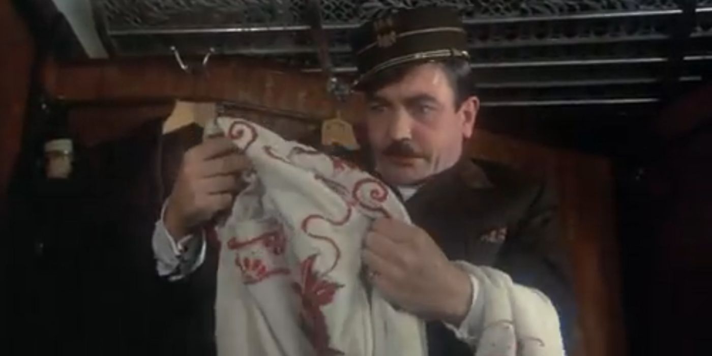 Hercule Poirot, dressed as a train conductor, examines a robe in Murder on the Orient Express.