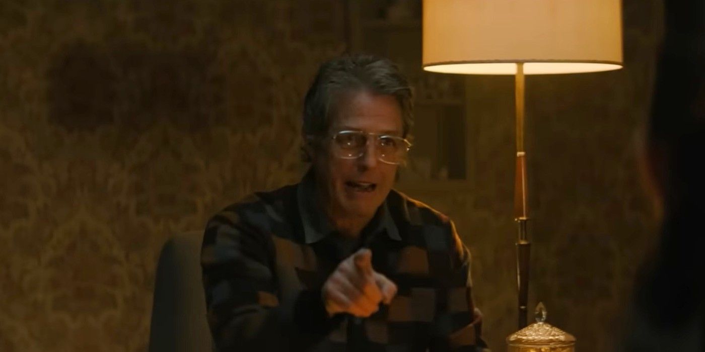 Hugh Grant as Mr. Reed pointing a finger towards the camera while sitting next to a lamp giving off yellow light in &lsquo;Heretic&rsquo;