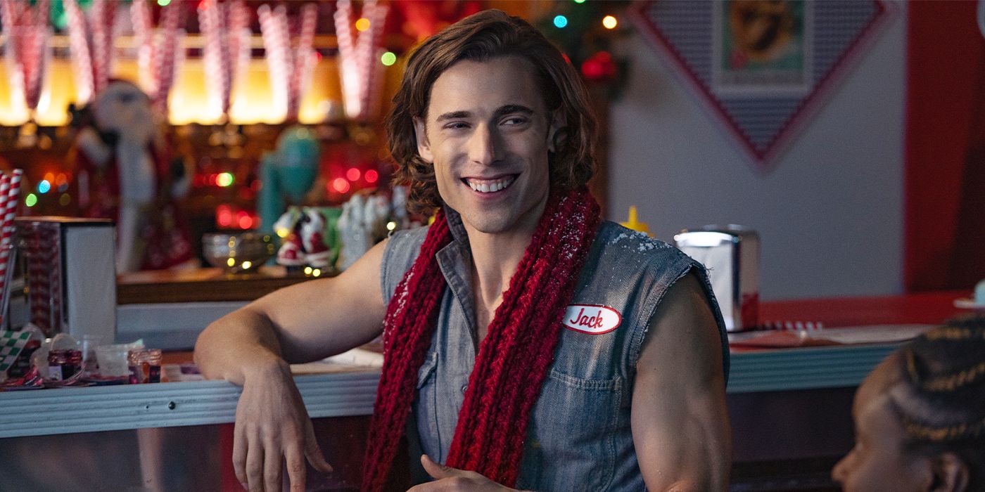 Dustin Milligan in a sleeveless jumpsuit and scarf smiling in a diner