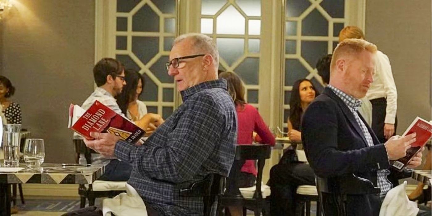 Jay and Mitch reading the same book, back to back, at separate tables in Modern Family
