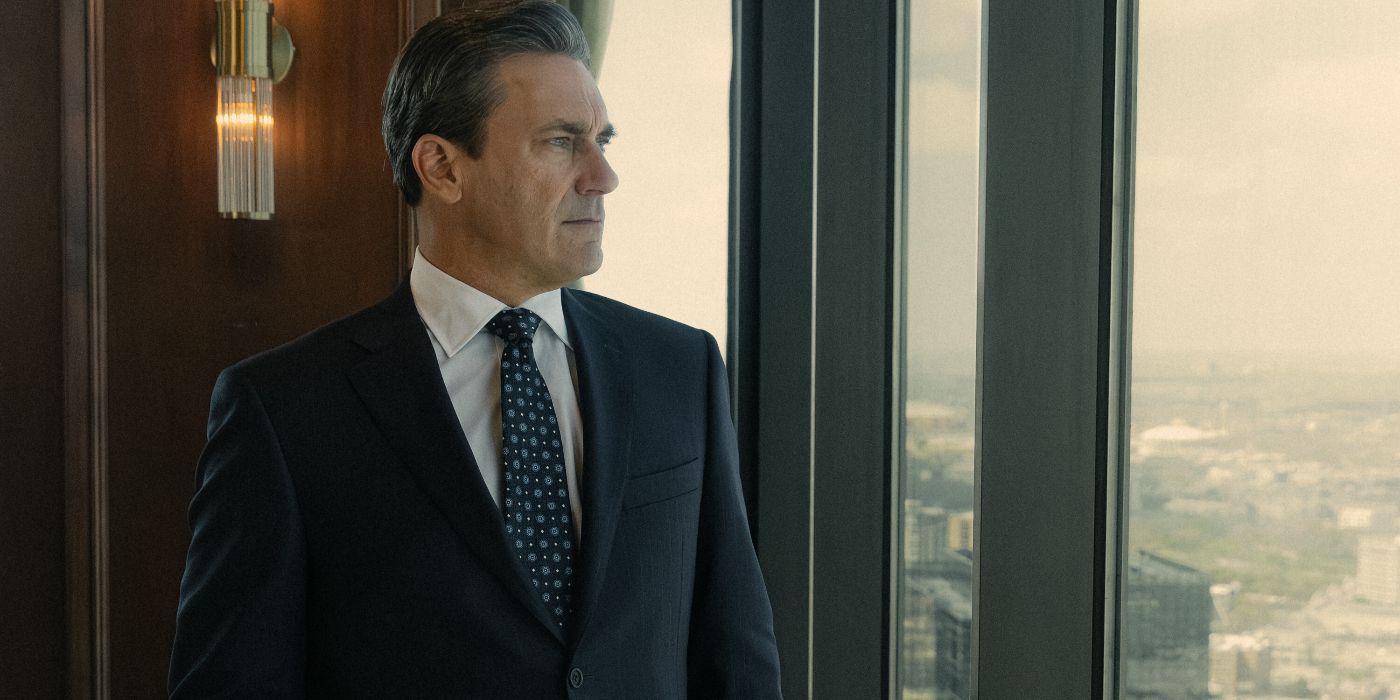 Monty Miller (Jon Hamm) wearing a dark navy business suit and tie and looking out a window toward the right in Landman