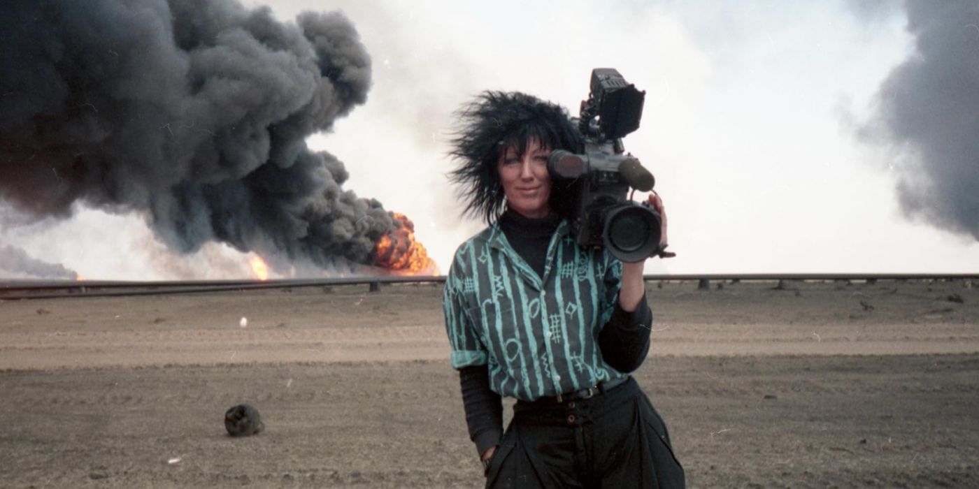 CNN Camerawoman Margaret Moth holds a camera while wearing a green and black striped shirt. Behind her, smoke billows from an explosion