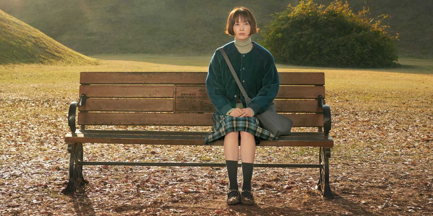 Lee Na-young sitting on a single bench in a park, surrounded by fallen leaves and green hills