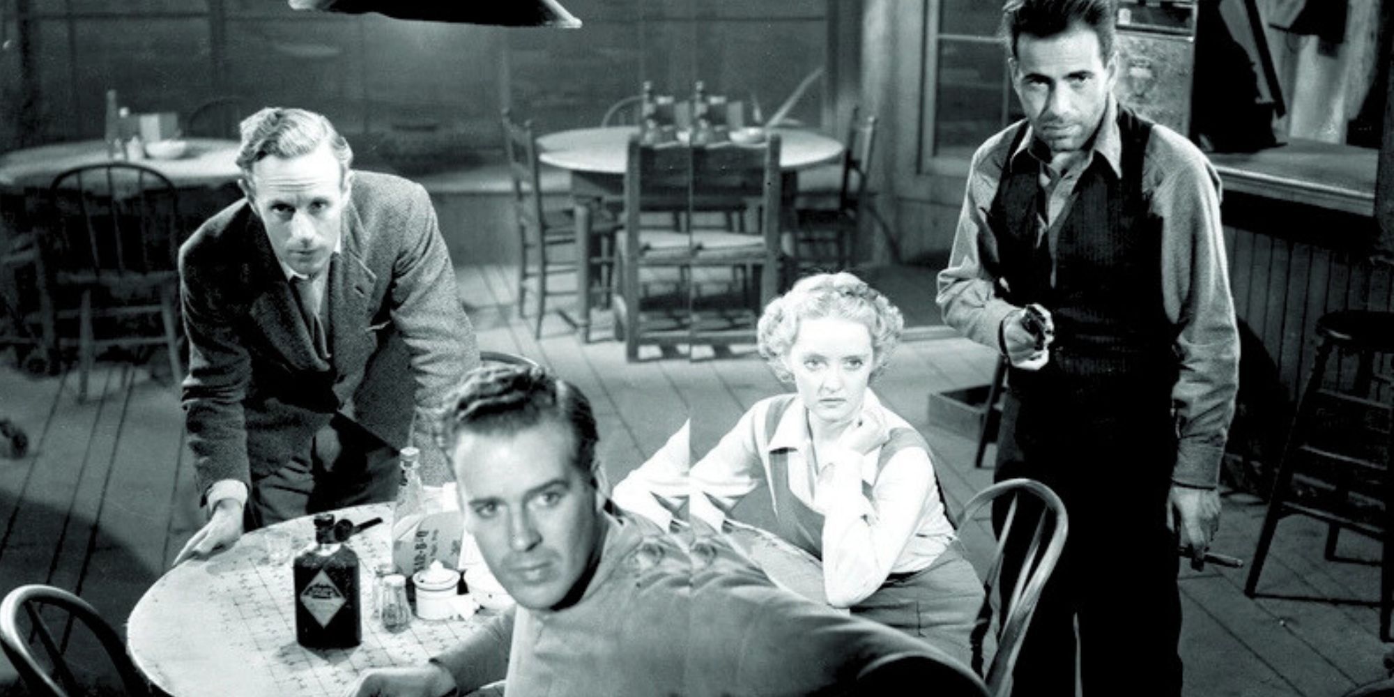 Leslie Howard leaning over a table, Bette Davis sitting next to him while Humphrey Bogart stands on the other side of her and Dick Foran sitting on the other side of the table in The Petrified Forest (1936)