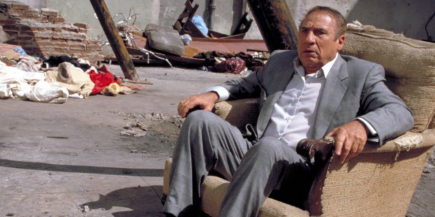 Mel Brooks sitting in a torn up chair wearing a suit in Life Stinks