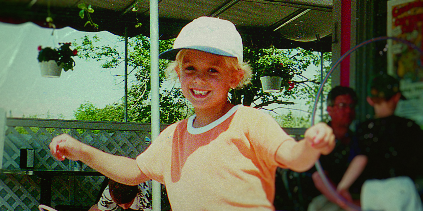 a smiling JonBenét Ramsey wears a baseball hat and orange shirt in archival footage from 'Cold Case: Who Killed JonBenet Ramsey'