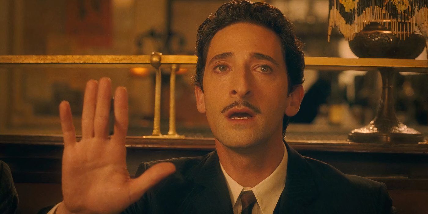 Adrien Brody as Salvador Dalí sits in a booth at a fancy restaurant in Midnight in Paris.