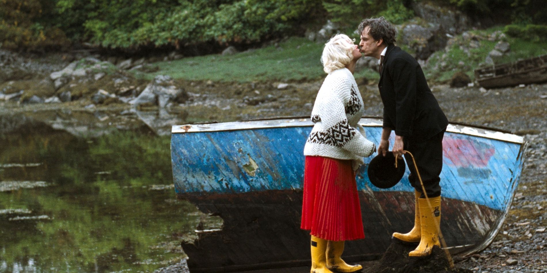 A Marilyn Monroe impersonator and a Charlie Chaplin impersonator wearing wellington boots and kissing next to a wooden boat in Mister Lonely.