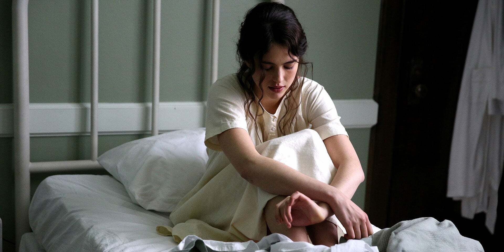 Margaret Qualley as Sister Cathleen sitting down in bed with a sorrowful look on her face in 'Novitate'