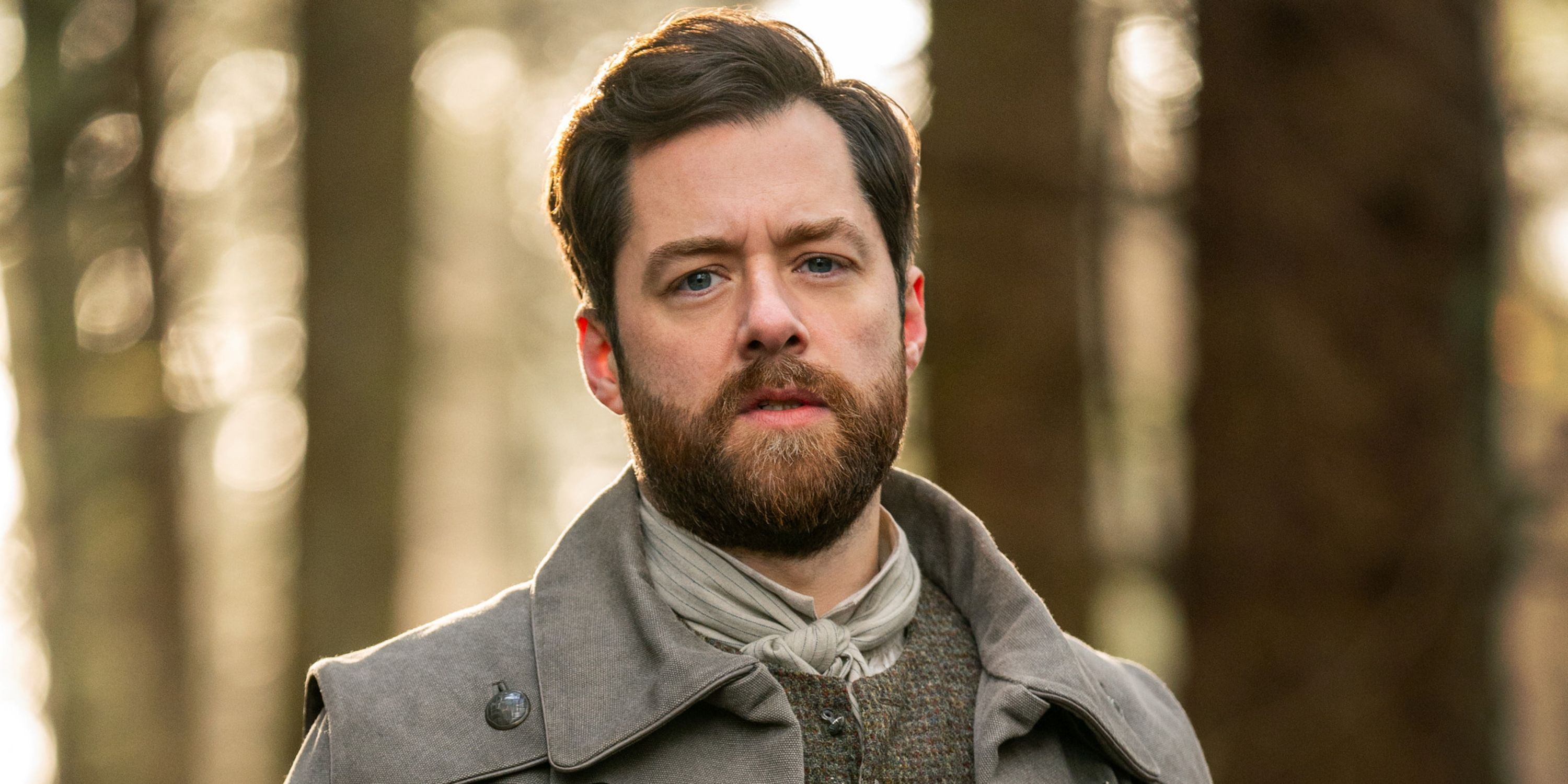 Richard Rankin as Roger Mackenzie in the forest looking into the camera for Season 7B of Outlander