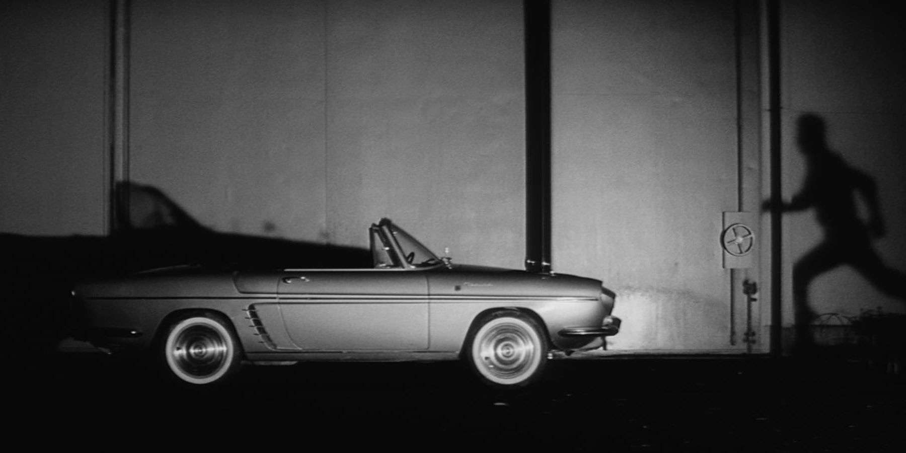 Muraki&rsquo;s shadow cast on a wall as he runs toward a car during a dream sequence in &lsquo;Pale Flower&rsquo;