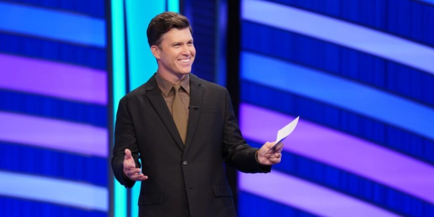 'Pop Culture Jeopardy' host Colin Jost smiling holding a question card