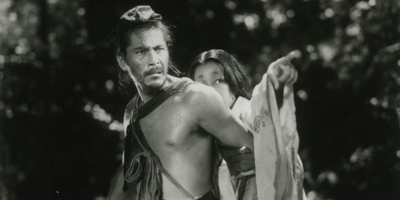 Tajōmaru (Toshiro Mifune), a rugged bandit, shields a woman who points over his shoulder in 'Rashomon' (1950).