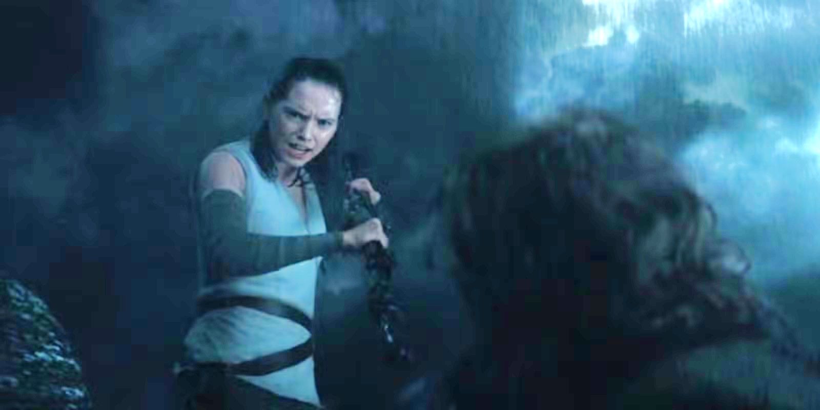 Rey (Daisy Ridley) aims a staff at Luke Skywalker (Mark Hamill) in the rain in Star Wars: The Last Jedi.