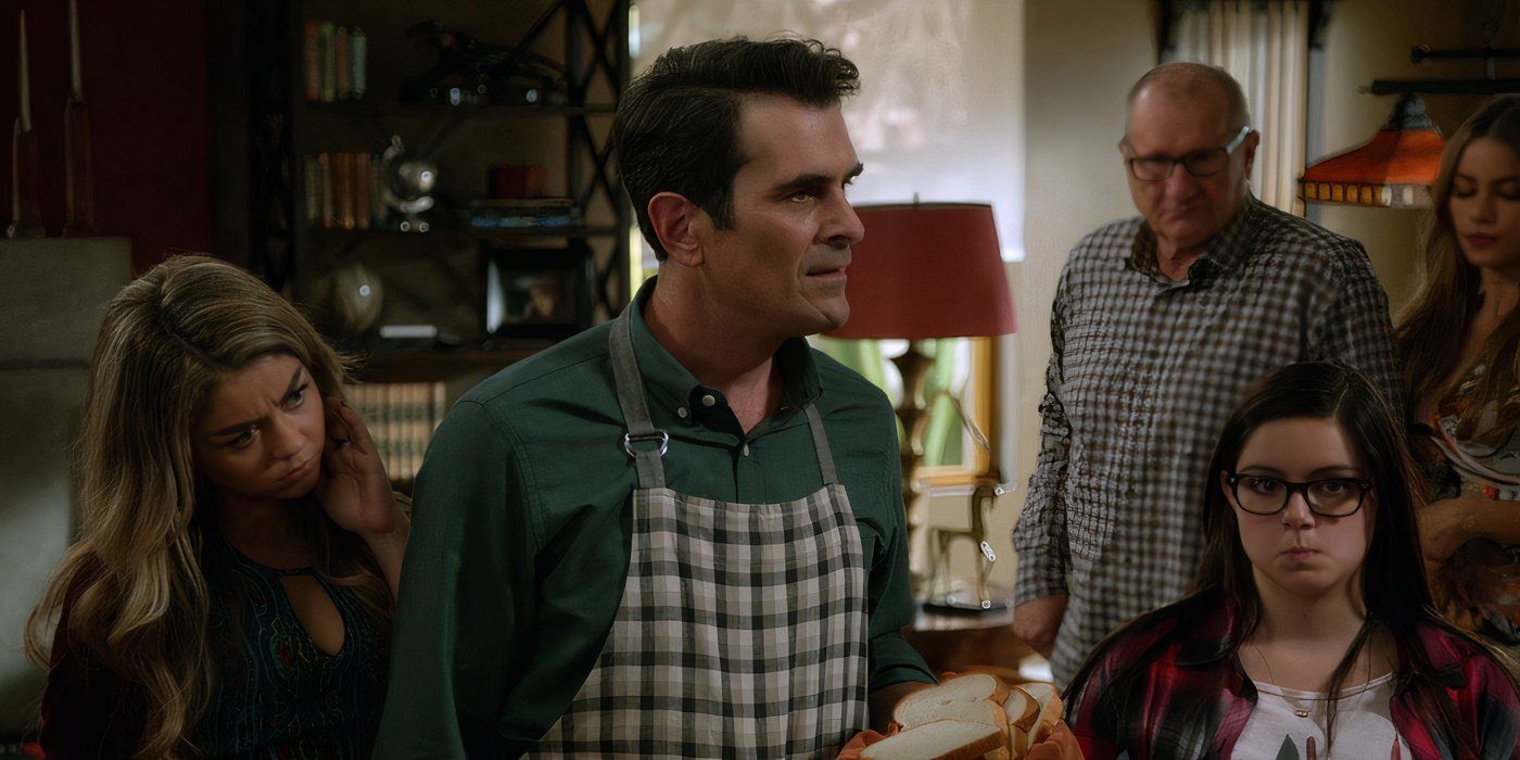 The Dunphys and the Pritchetts stand in the living room in Modern Family.