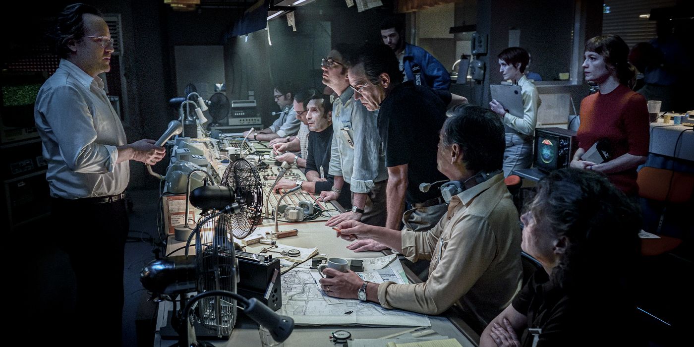 People sitting and standing around a control room listening to Roone Alredge (Peter Sarsgaard) speak