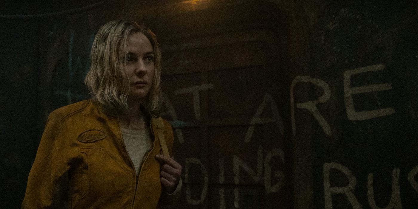 Juliette Nichols (Rebecca Ferguson) wearing a white shirt under a yellow jacket and carrying a bag over her shoulder walking past a graffiti-covered wall in Silo Season 2