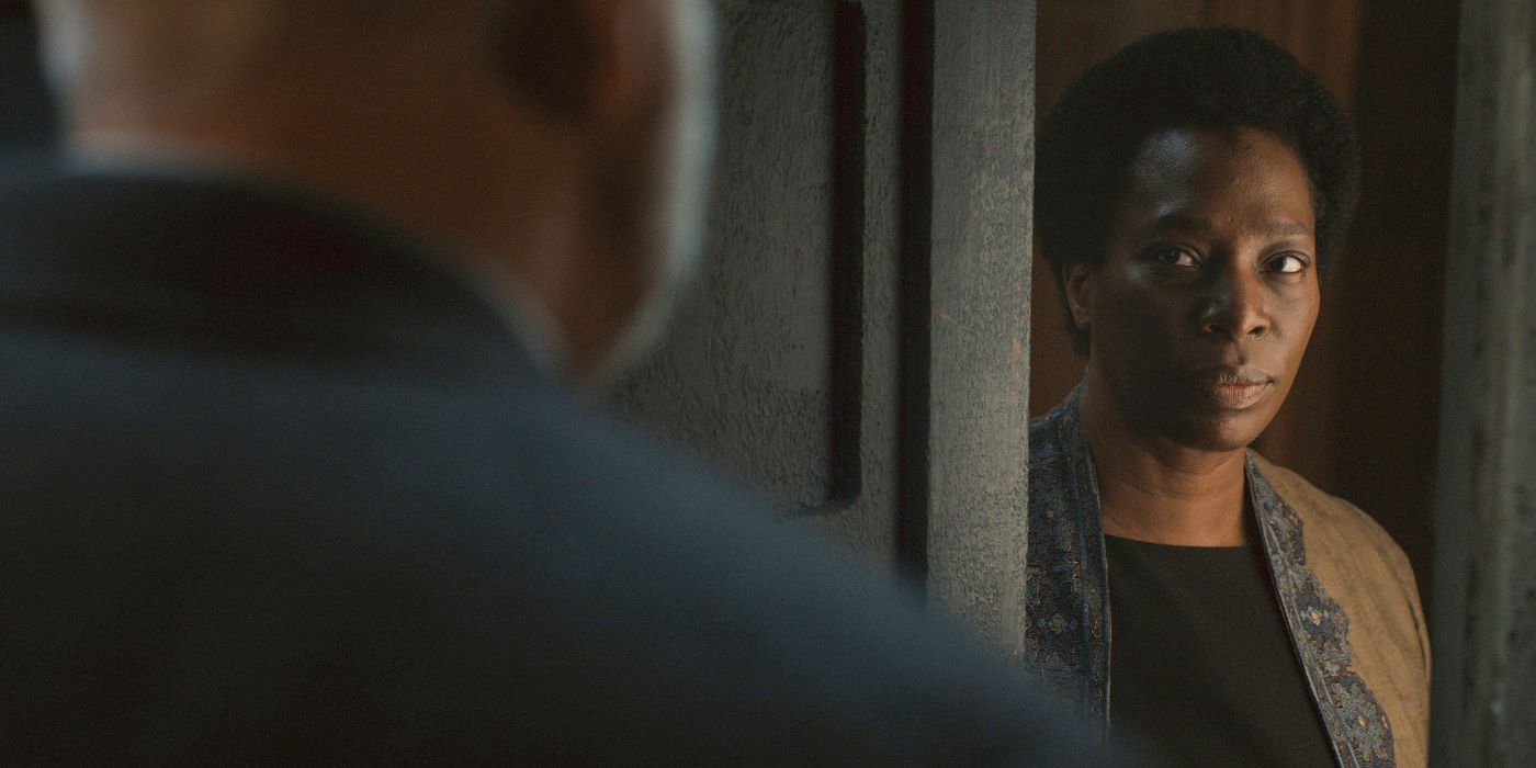 Judge Meadows (Tanya Moodie) looking out her open door at Bernard Holland (Tim Robbins), who stands at her threshold and is seen over the shoulder, in Silo Season 2