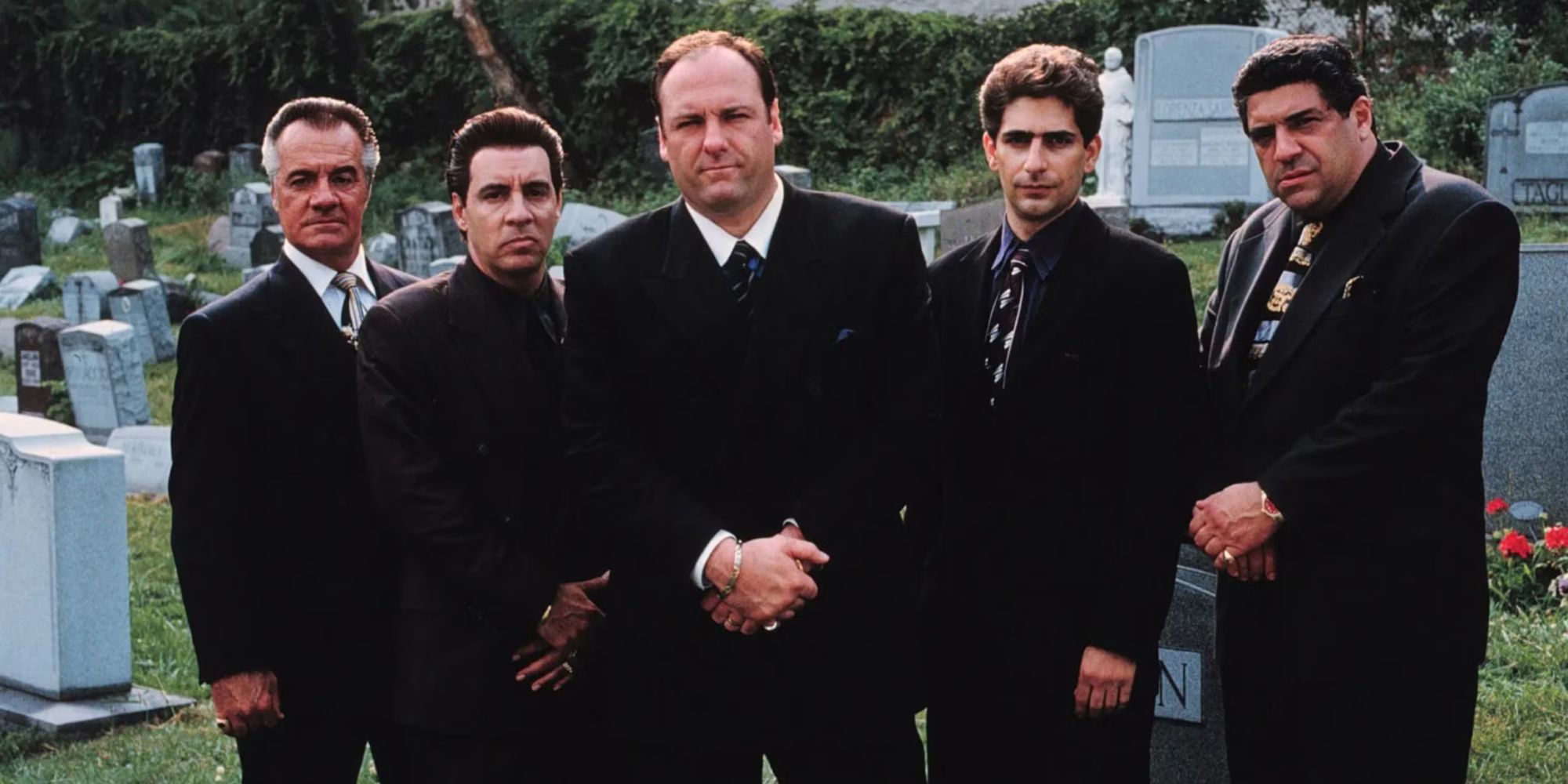 The cast stand together looking somber in black suits in a graveyard in The Sopranos.