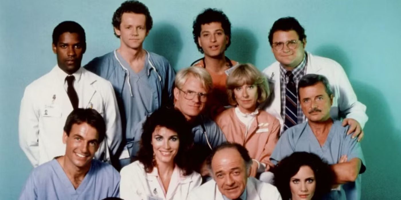 The cast of St. Elsewhere pose for a photo together against a plain blue backdrop.