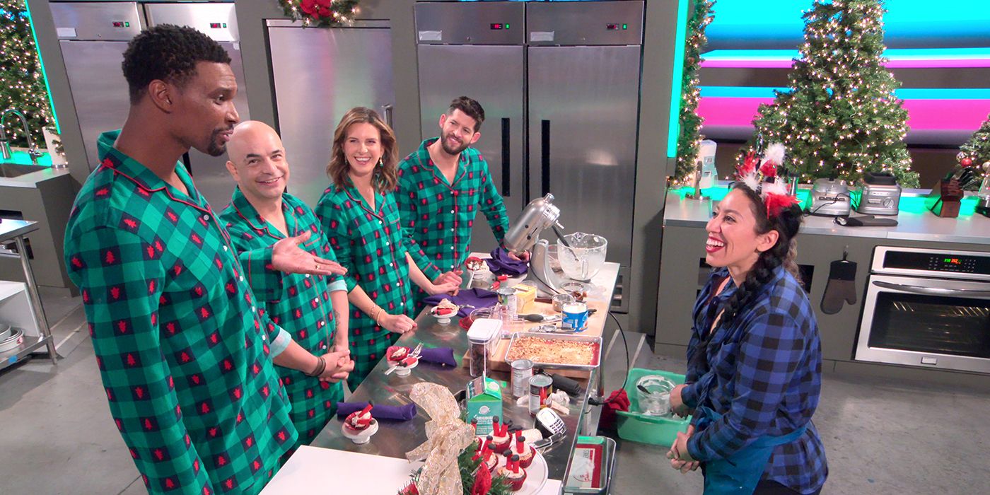 A woman talks on one side a counter to four others in matching red and green pyjamas in Sugar Rush Christmas.