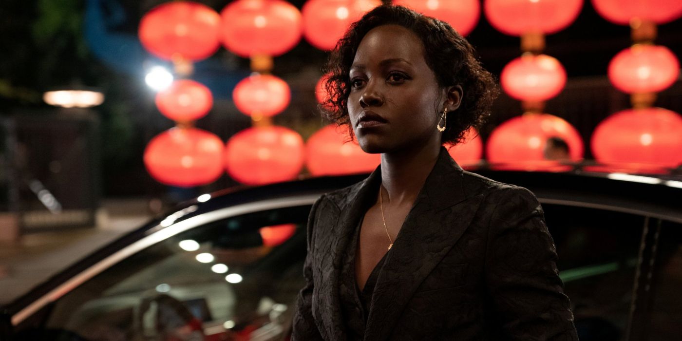 Khadijah Adiyeme (Lupita Nyong&rsquo;o) wears a black suit jacket as she walks past a shiny black car in front of a display of red lights in &lsquo;The 355&rsquo; (2022).