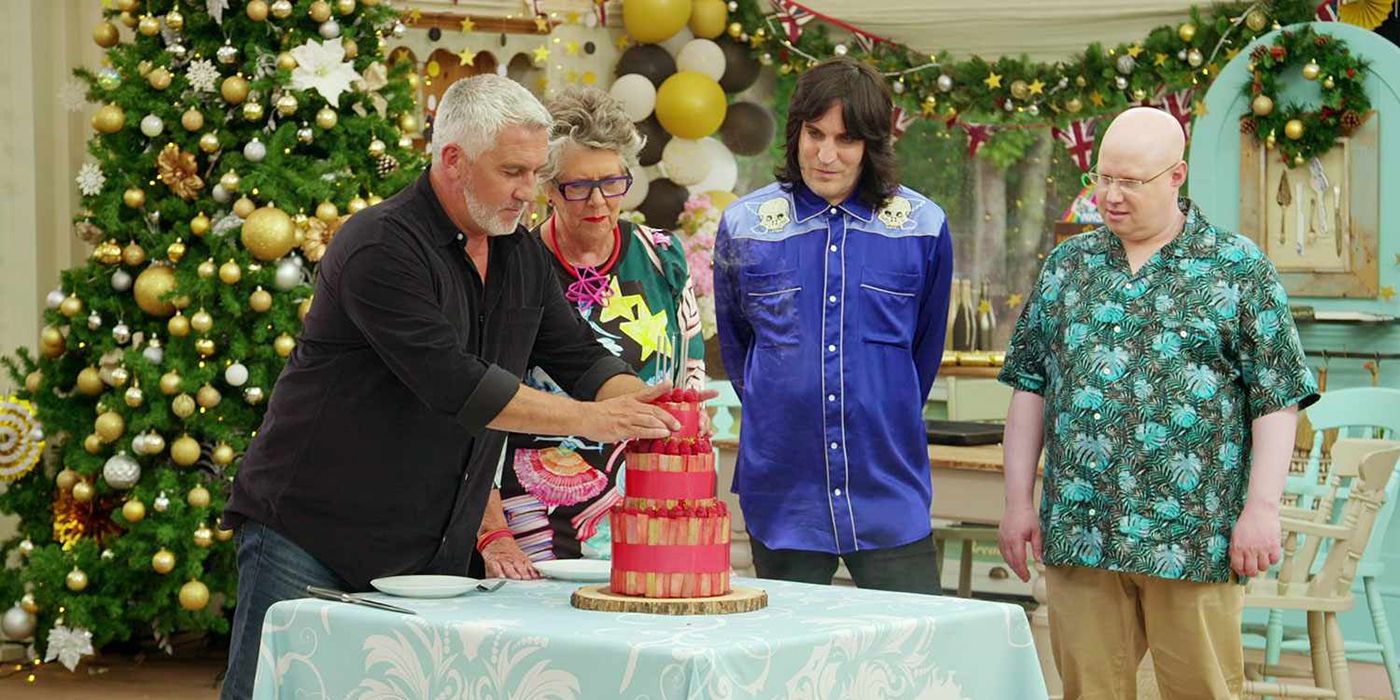 The judges and Paul Hollywood look over a tiered cake from a competitor in The Great Holiday Baking Show.