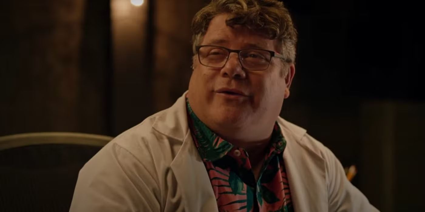 Sean Astin wearing a lab coat and smiling in The Invisible Raptor