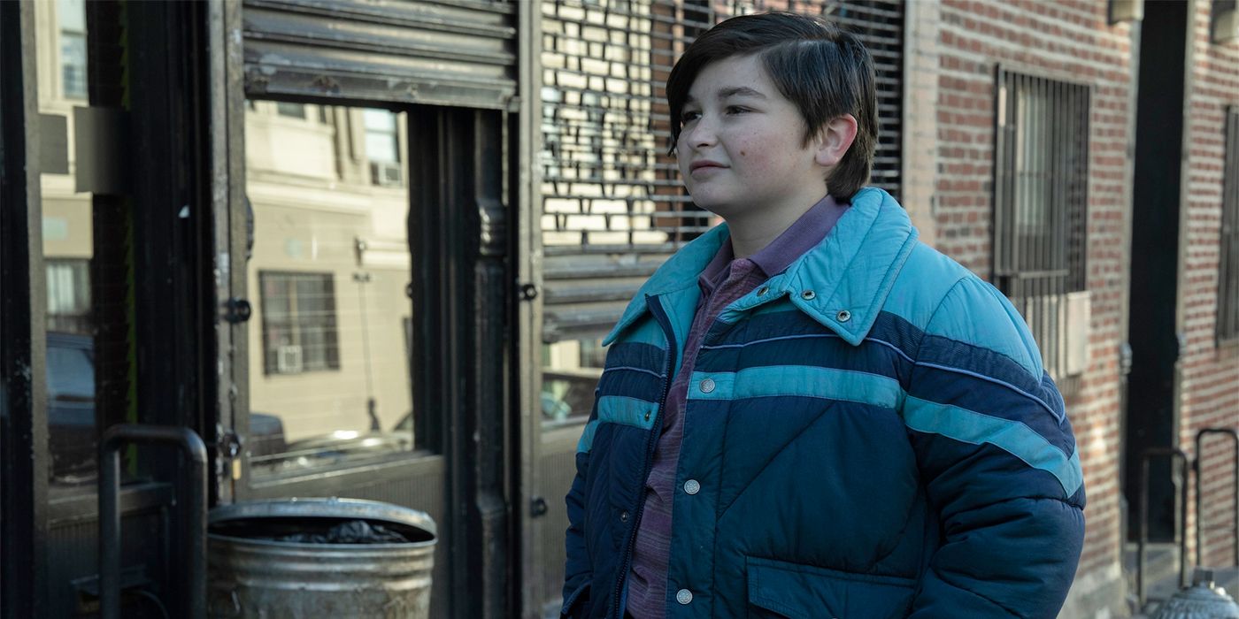 Ryder Allen as the young Oz Cobb in a blue puffy jacket smiling in The Penguin