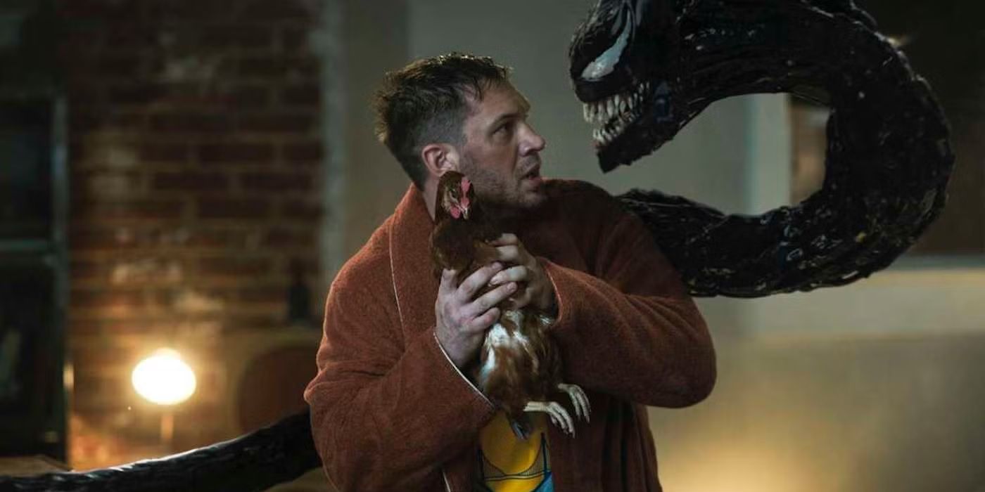 Tom Hardy holds a chicken as Venom comes from behind and faces him in Venom: Let There Be Carnage.