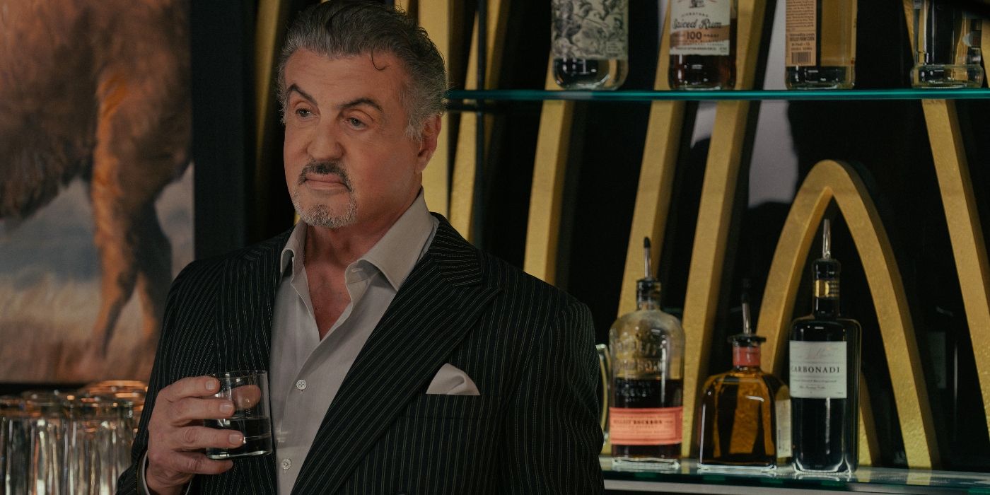 Sylvester Stallone holding a drink and standing behind a bar