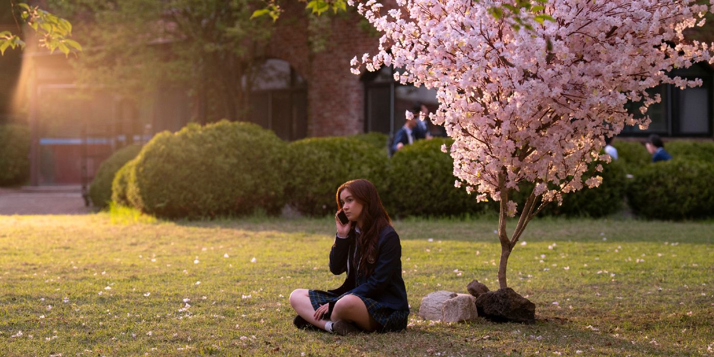 Anna Cathcart sits and takes a phone call in front of a cherry blossom in XO, Kitty Season 2