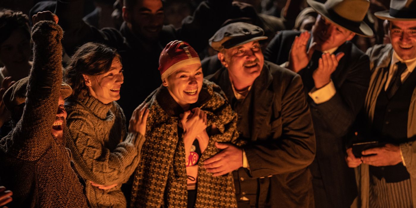 Trudy Ederle (Daisy Ridley) standing in a crowd of people at night smiling and wrapped in a blanket