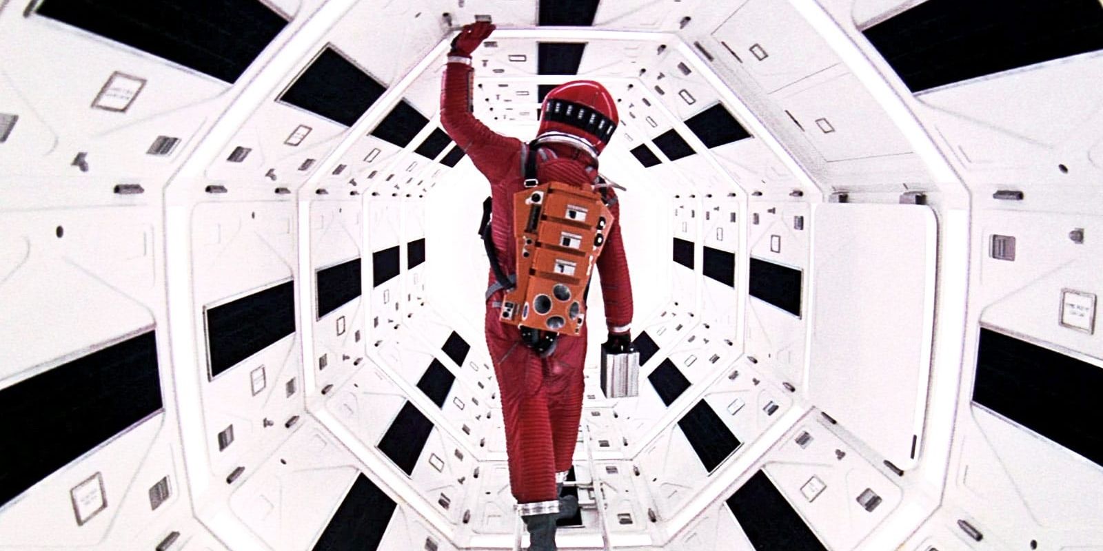 Keir Dullea in a red spacesuit walking through well-lit space pod in 2001: A Space Odyssey.