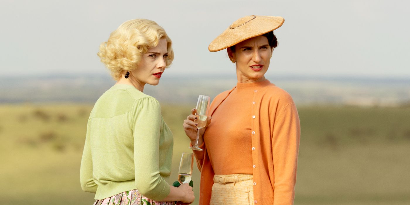 Lucy Boynton and Bessie Carter staring with disdain while holding champagne glasses