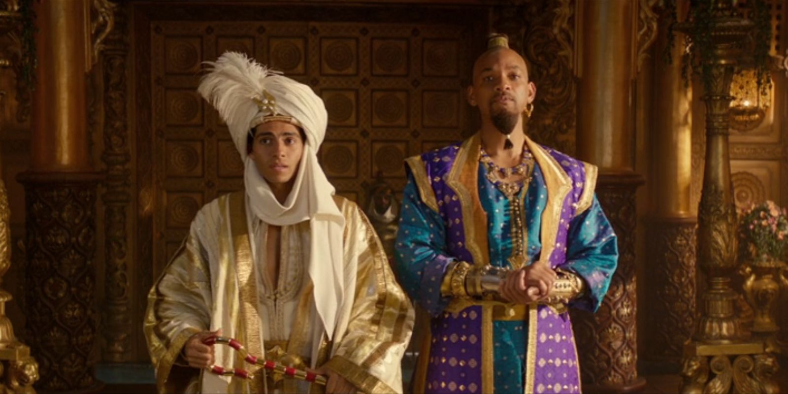 Aladdin, played by Mena Massoud, and Genie, played by Will Smith, stand side-by-side in royal attire in 'Aladdin'.